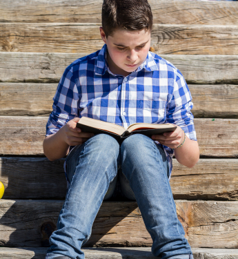 Young boy reading a book in the woods with shallow depth of fiel